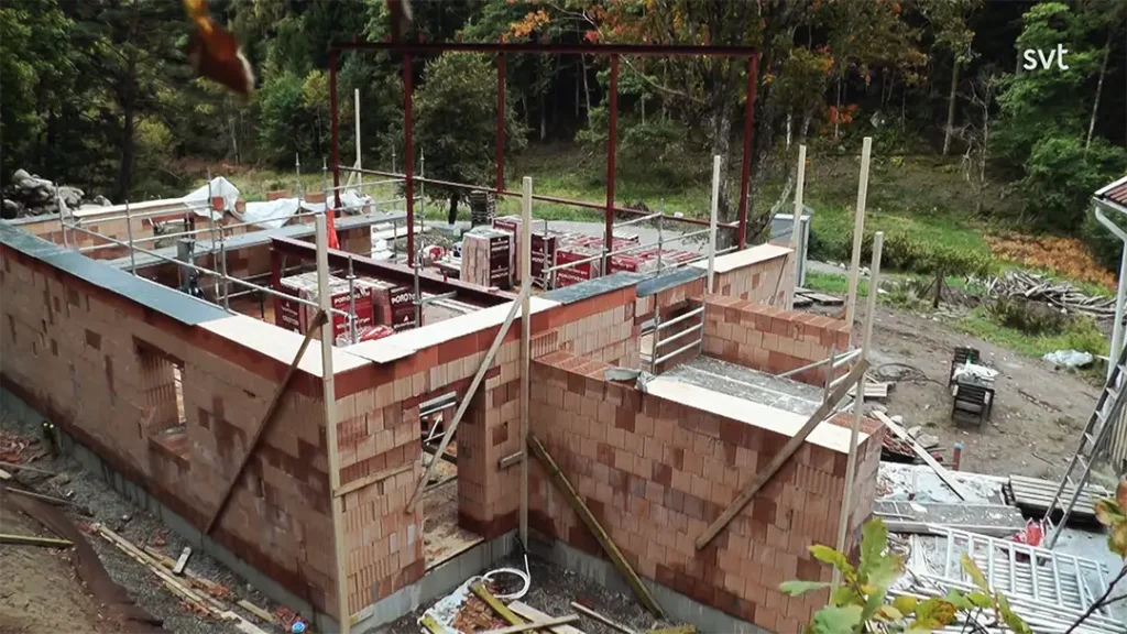 Stiligt - En delvis byggd tegelbyggnad med exponerad stålram, byggmaterial och byggnadsställningar på en lantlig utomhustomt.