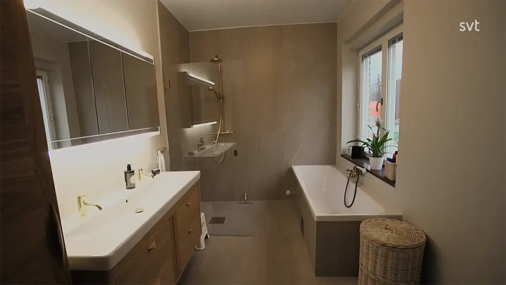 Stiligt - Modernt badrum inspirerat av Lund - Husdrömmar, med dubbelt handfat, vägghängda skåp, duschkabin, badkar vid fönstret, eleganta guldarmaturer och en snygg flätad tvättkorg.