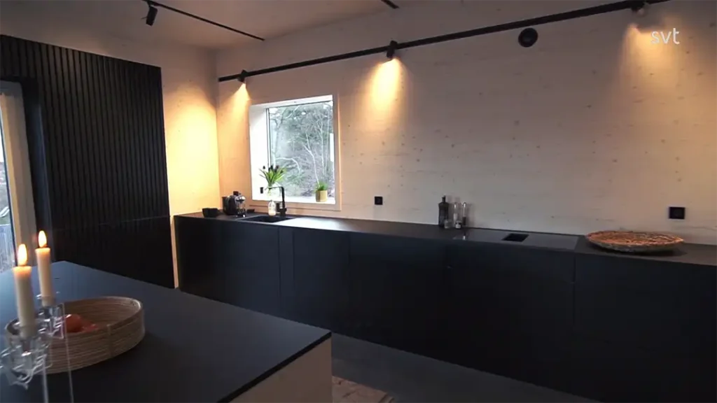 Stiligt - Modernt minimalistiskt kök med svarta skåp, ett fönster, bänkskivor och en pizza på bänken – klassisk Västra Frölunda – Husdrömmar stil – plus ljus på ett bord i förgrunden.