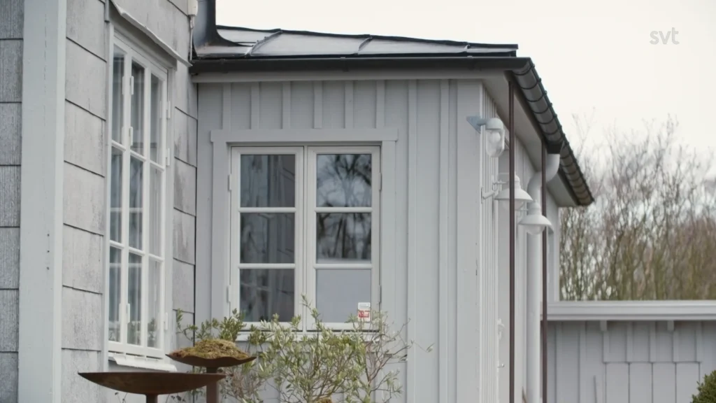 Stiligt - Ett ljusgrått trähus med vita inramade fönster, svart tak, och fågelmatare med frön i förgrunden framkallar charmen hos Västra Klappe - Husdrömmar.