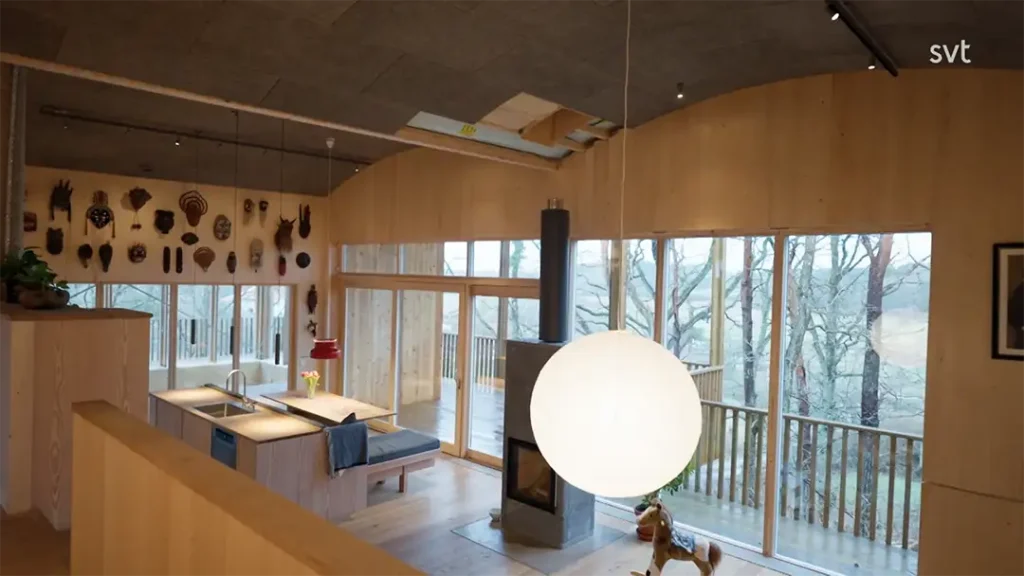 Stiligt - Modernt träkök och matplats inspirerat av Onsala - Husdrömmar, med stora fönsterpartier, en central rund hänglampa, väggmonterade dekorationer och utsikt över träd utanför.