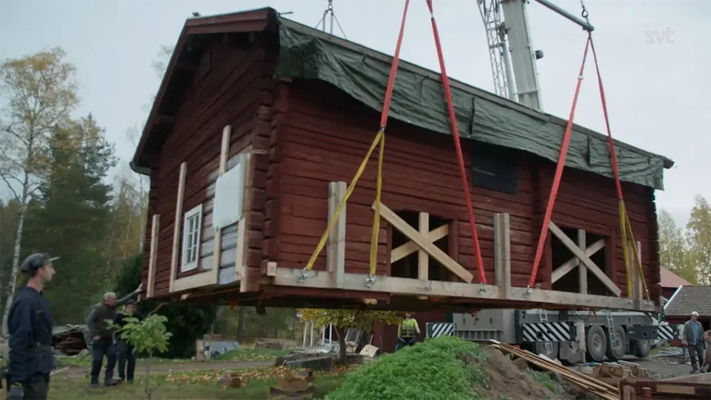 Stiligt - Ett rött trähus i Stråtenbo lyfts av en kran med röda remmar, medan flera personer iakttar den Husdrömmar-inspirerade processen utomhus.