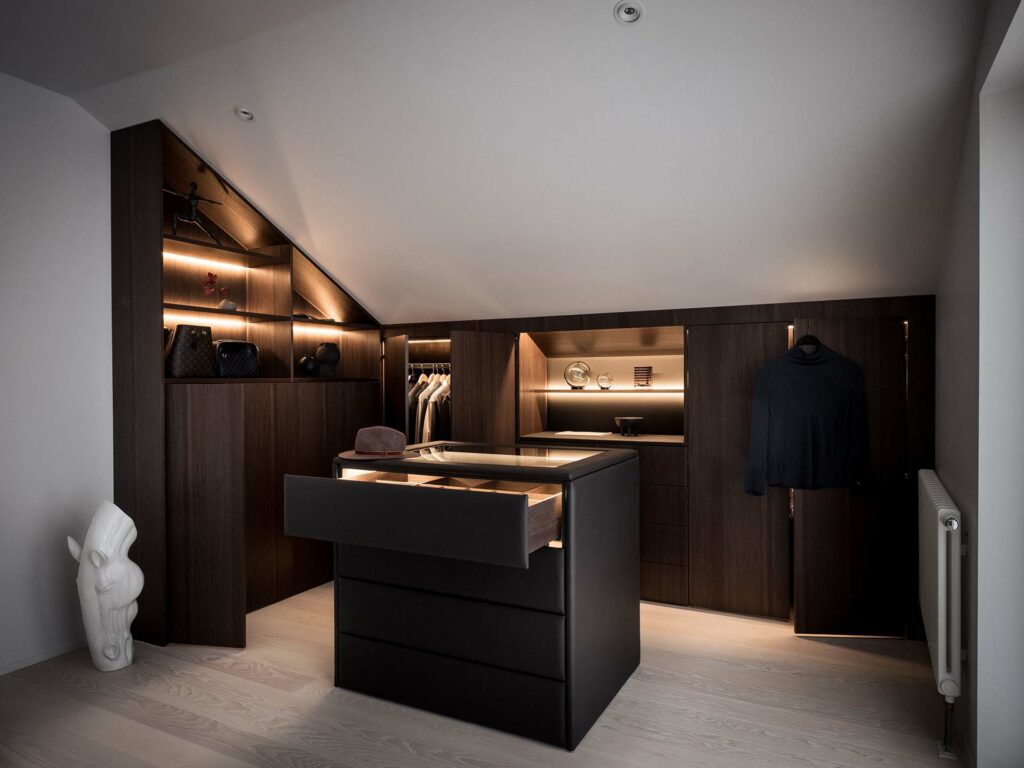 Stylish - A classy, luxurious walk-in closet with dark wood details, shelves adorned with stylish bags and shoes, hanging clothes elegantly arranged and a central island bathed in soft lighting.