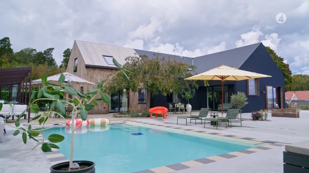 Stiligt - Modernt Onsala-hus med trä och mörka fasader, en pool, utemöbler, poolflottor, paraply och omgivande träd under en molnig himmel - en inspirerande tillflyktsort i Grand Designs.