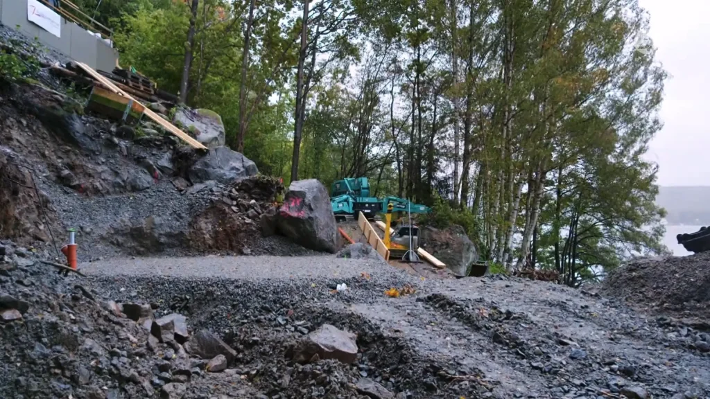 Stiligt - En byggarbetsplats i ett skogsområde nära Borås – Grand Designs-stil – med stenar, grus och entreprenadutrustning synligt runt slående träkonstruktioner.