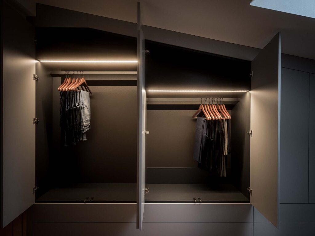 Stylish - Open modern wardrobe with stylish LED lighting, showcasing pants and shirts hanging on wooden hangers inside two cabinets.