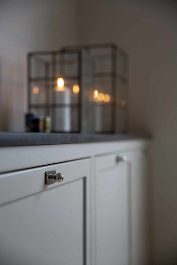 Stylish - A dimly lit, stylish room has a white cabinet adorned with two tall glass lanterns, each holding a soft flickering light on top.