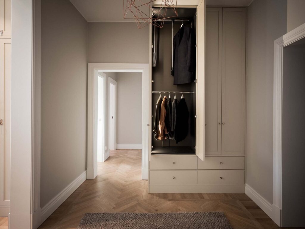 Stylish - A stylish, well-organized wardrobe with open doors reveals hanging clothes and drawers that perfectly complement the minimalist room's wooden parquet floor and neutral walls.