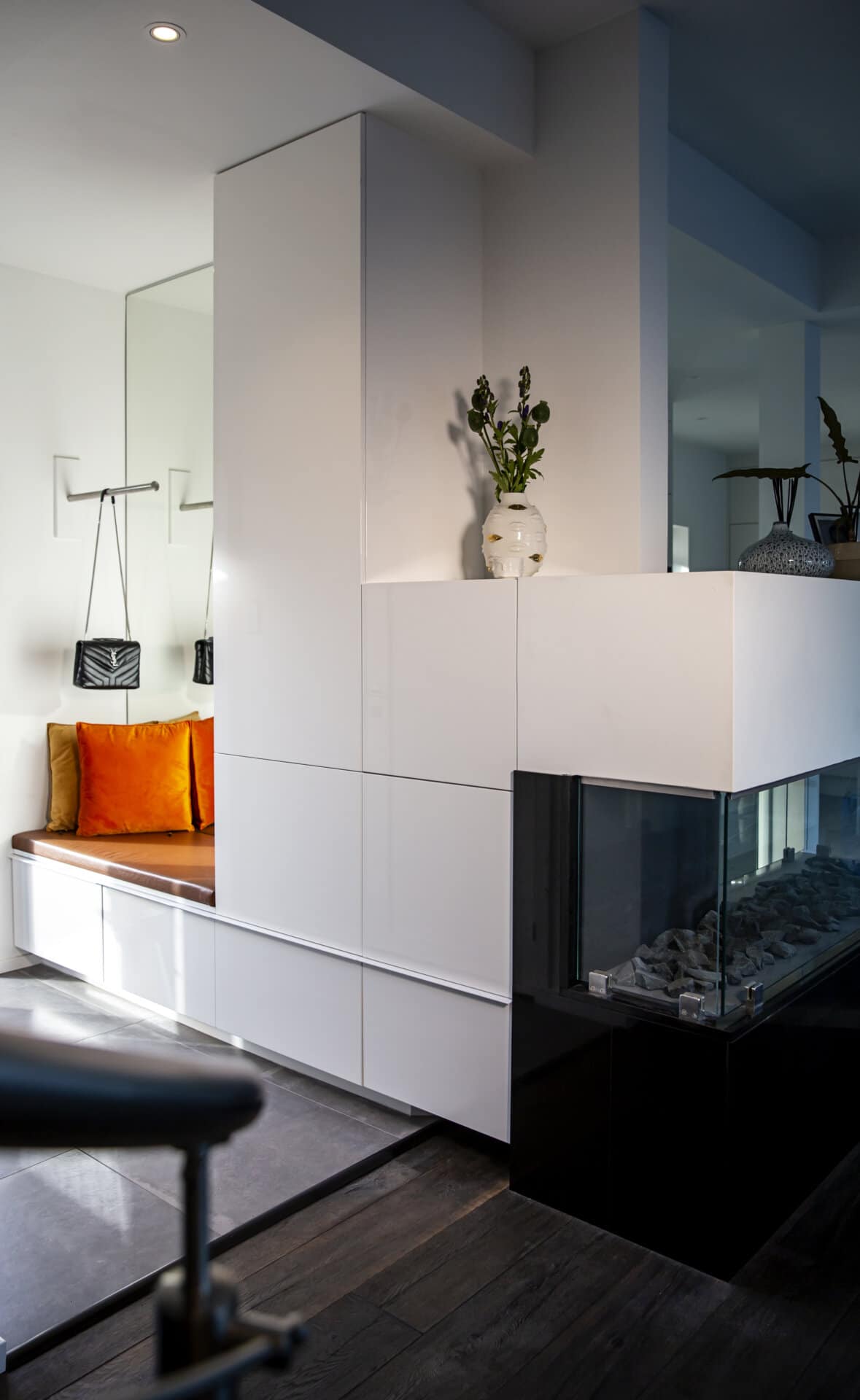 Stylish - A stylish modern living room showcases a sleek white built-in unit, complemented by a glass fireplace. The small seating area is adorned with vibrant orange cushions and a decorative vase topped with lush foliage, creating an inviting atmosphere.