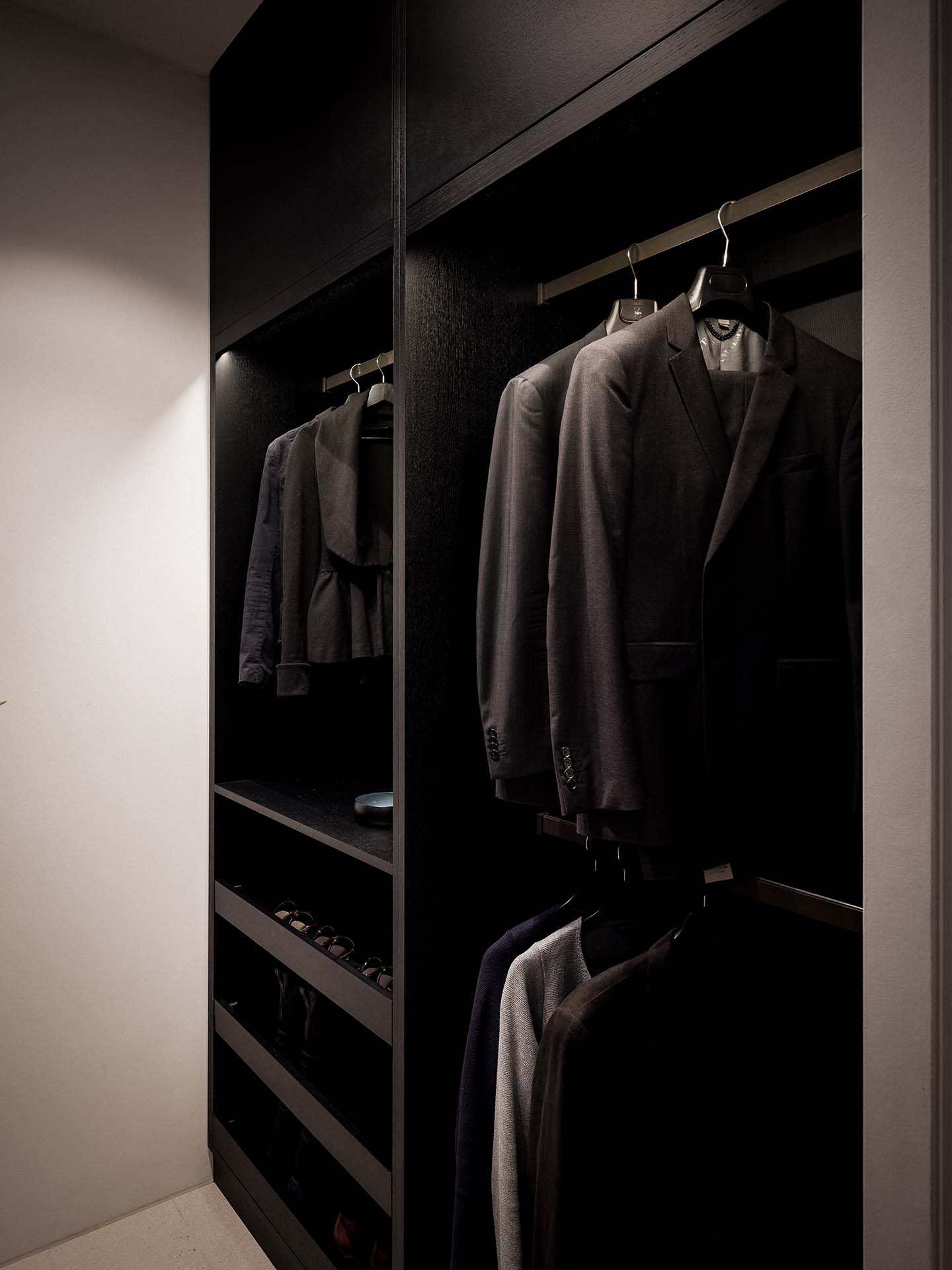 Stiligt - En svagt upplyst Liten walk in closet med flera stiliga mörka kostymer hängande prydligt på galgar, bredvid hyllor med par skor och accessoarer.