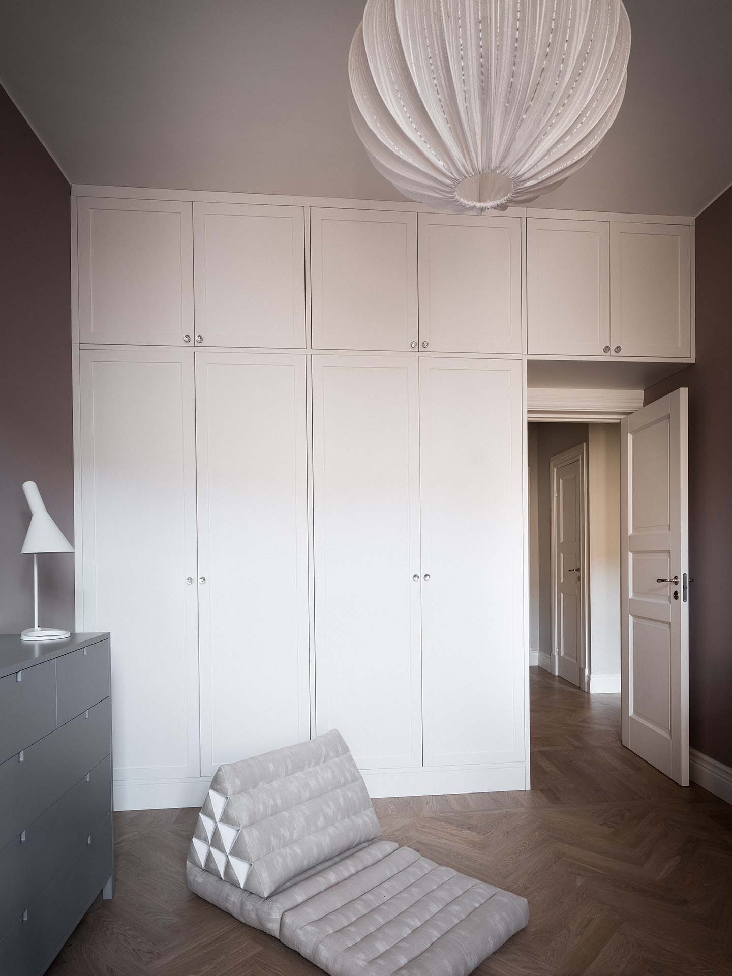 Stylish - Hallway storage in warm gray shaker-style wardrobes, a gray dresser, a white lamp and a folding chair on a wooden floor.