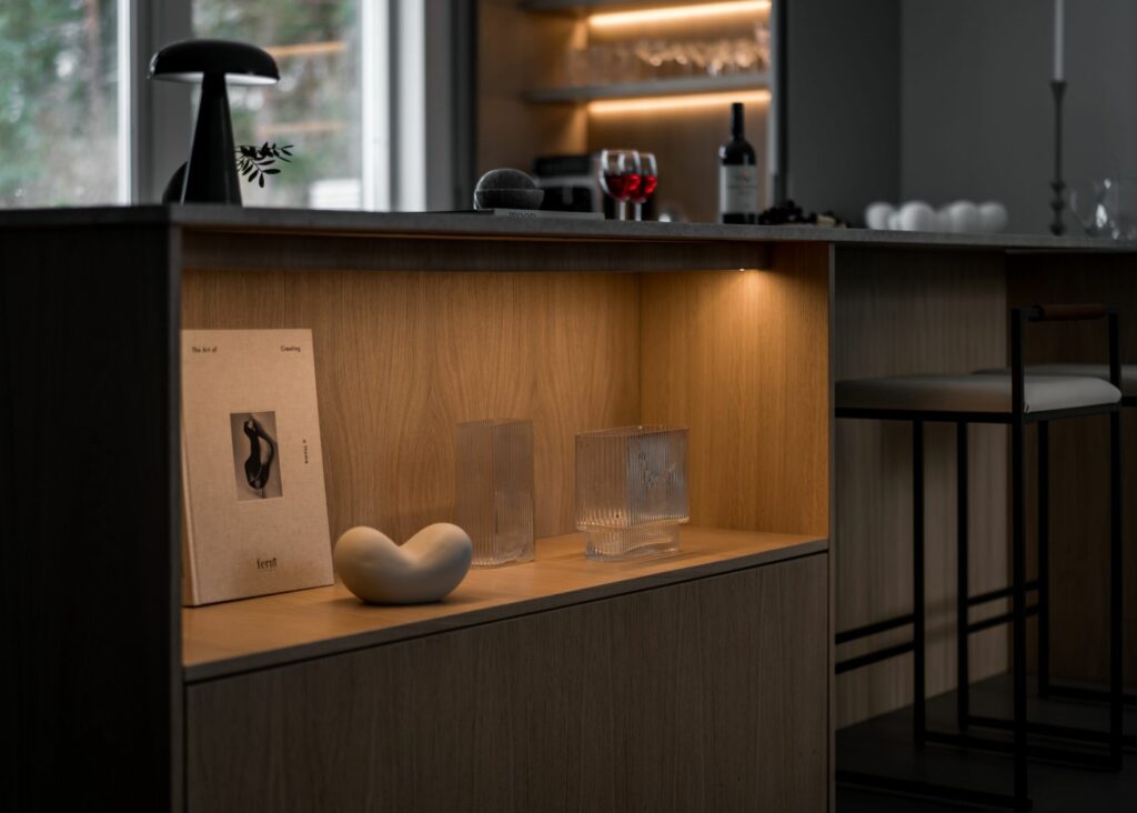 Stylish - A stylish modern kitchen showcases a wooden island adorned with decorative items, a glass of red wine and a bottle in the background. A stylish black stool stands nearby.