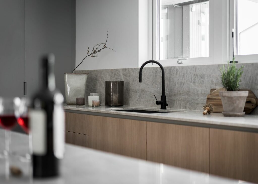 Stylish - Minimalist kitchen with stylish light wood cabinets, an elegant black faucet, decorative plants and a wine bottle elegantly placed on the counter.