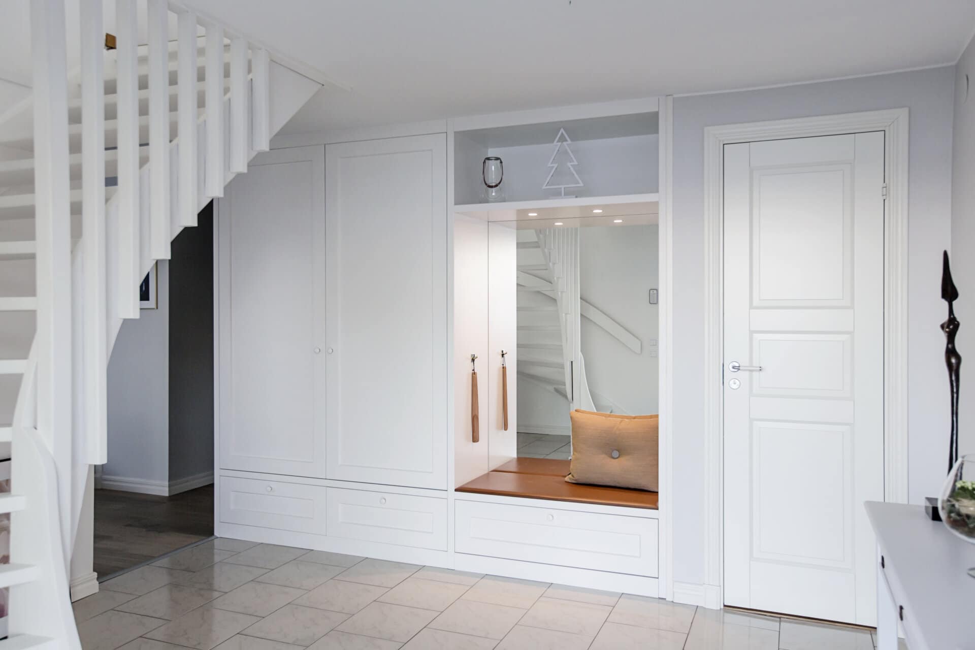 Stylish - Stylish minimalist hallway with white built-in cabinets, a wooden bench with cushion and a decorative mirror. A staircase is visible on the left.