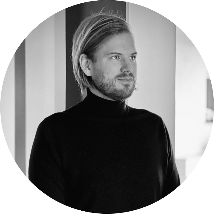 Handsome - A person with shoulder-length hair and a beard, exuding a handsome appearance, wears a black turtleneck. They are standing next to a wall and looking sideways in this striking black and white image.