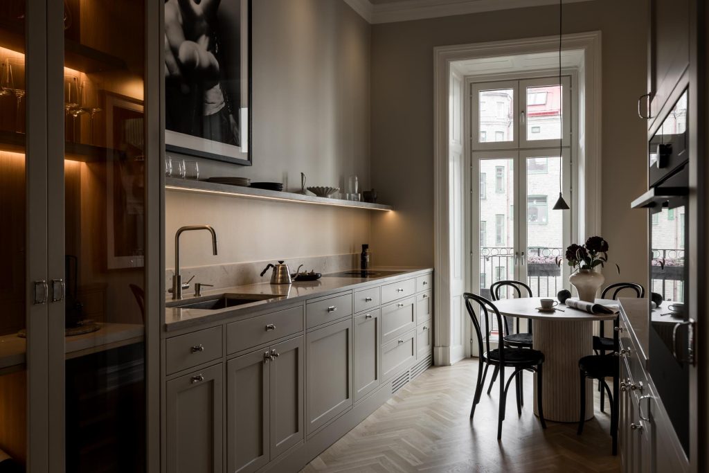 Stylish - A modern stylish kitchen with bright cabinets, a built-in oven and a round dining table along with black chairs. A large window welcomes natural light while art decorates the wall elegantly.