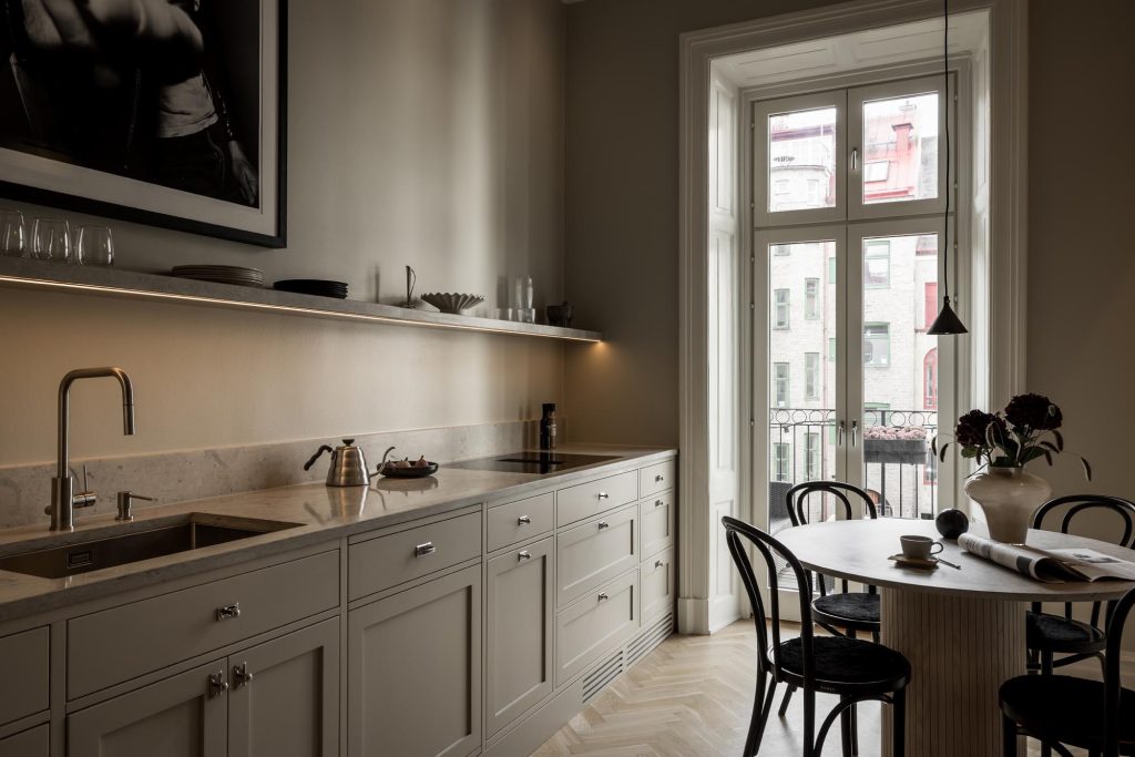 Stylish - A stylish, minimalist kitchen with light gray cabinets, a marble countertop and a round dining table with chairs. The space is enhanced by a large window that floods the room with natural light.