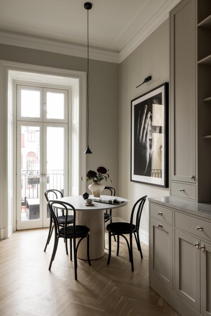 Stylish - A modern dining area features a stylish round table, four black chairs, a hanging ceiling light and a striking black and white photograph. Large windows allow natural light to elegantly fill the room.
