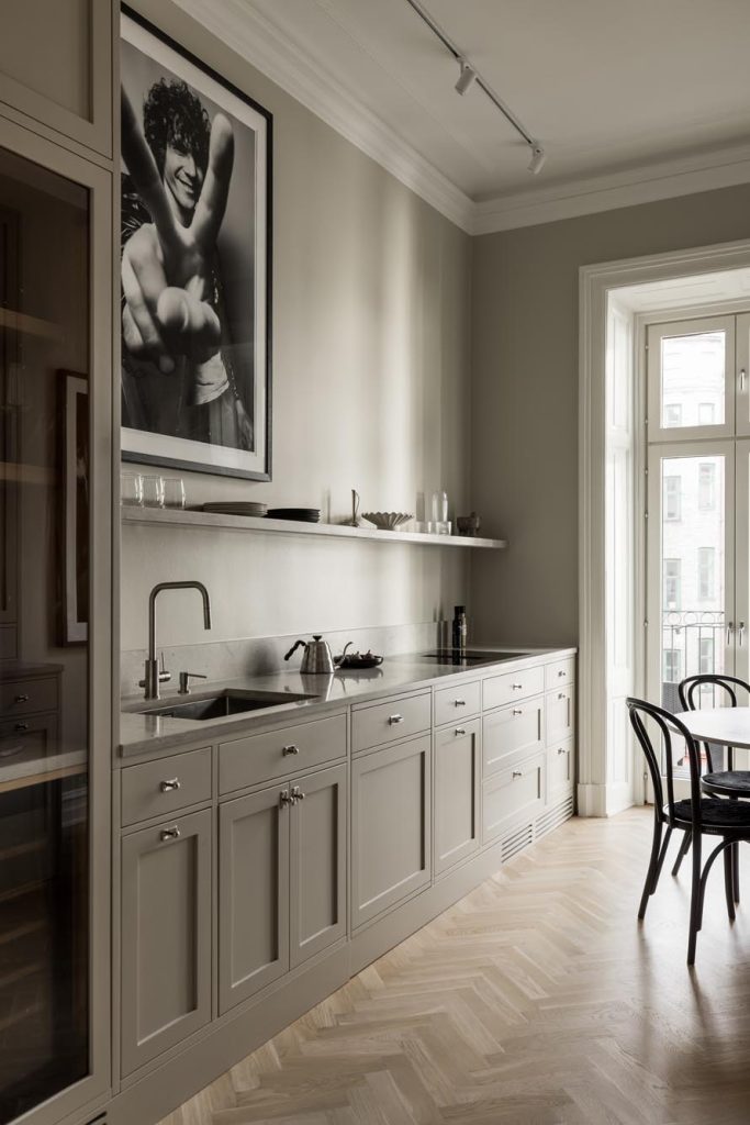 Stylish - Modern kitchen with light gray cabinets, sleek countertops and a framed black and white photo on the wall. A stylish touch is added by the large window and the dining room with elegant black chairs in the background.