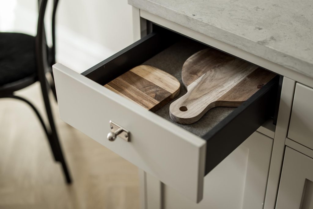 Stylish - Open the kitchen drawer to find two handsome wooden cutting boards nestled inside, next to a chair and a sleek gray countertop.