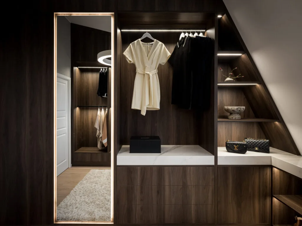 Stiligt - En modern klädkammare med mörka trähyllor, hängande kläder och hyllor för lådor och väskor. Den stora vertikala spegeln framhäver spegelns funktion i walk in closet genom att förstärka utrymmet och lägga till elegans.