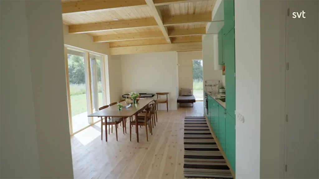 Stylish - A bright, minimalist dining area with hardwood floors, green kitchen cabinets and large windows overlooking a grassy outdoor scene that captures the airy elegance of Sandby - House Dreams style.