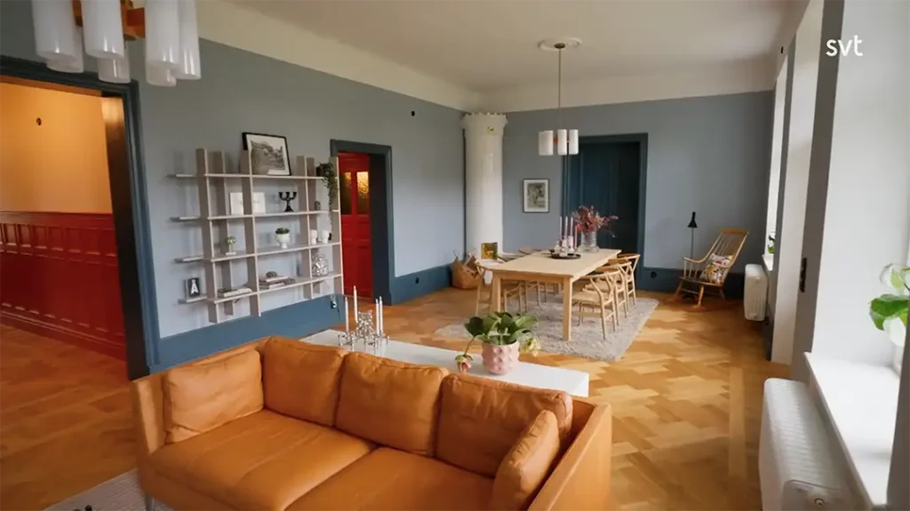 Stiligt - Ett rymligt vardagsrum och matsal med ljusblå väggar, trägolv, en brun soffa, ett matbord med stolar, hyllor och stora fönster som släpper in naturligt ljus.
